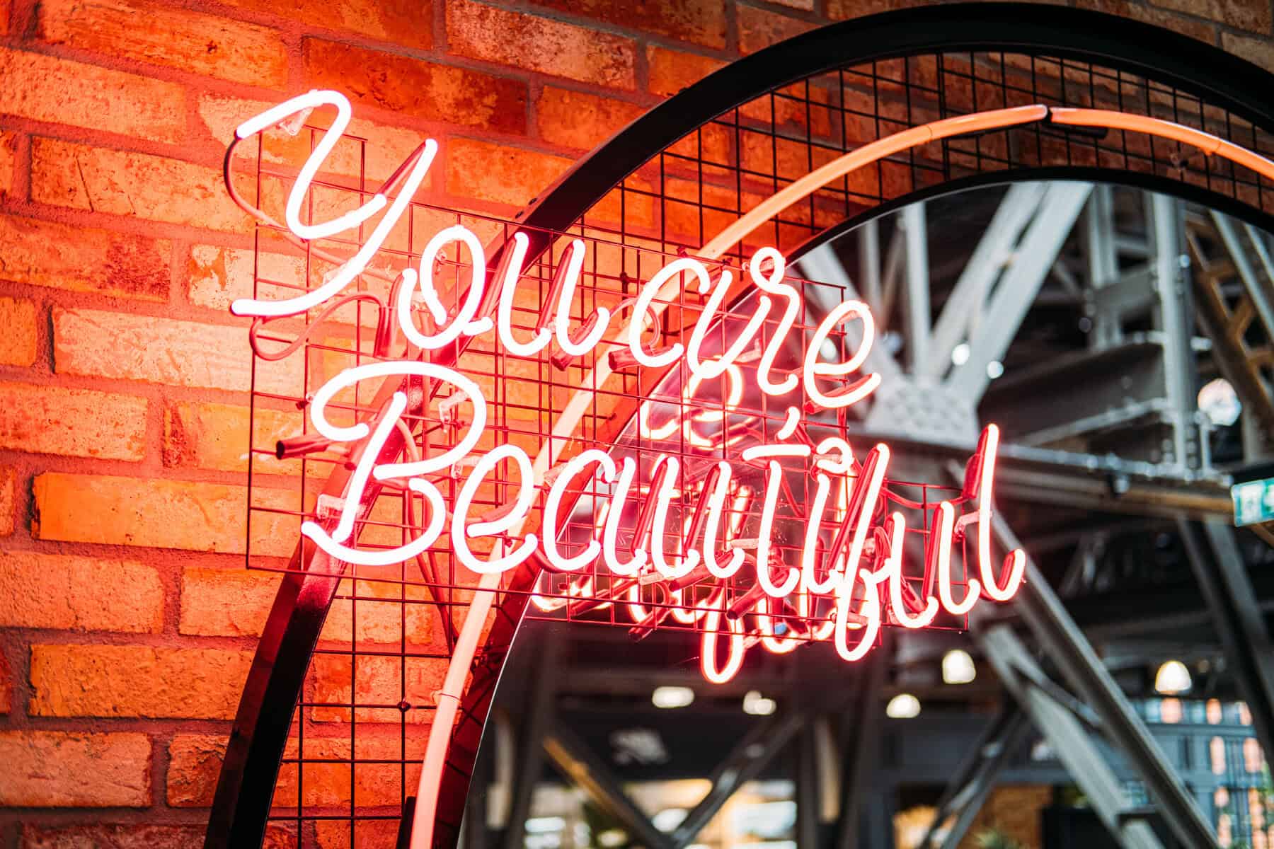 Neon "You’re Beautiful" sign on rustic brick wall, perfect for interior decor and modern design.